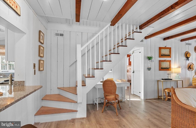 stairs with sink, wood-type flooring, beam ceiling, and wooden walls