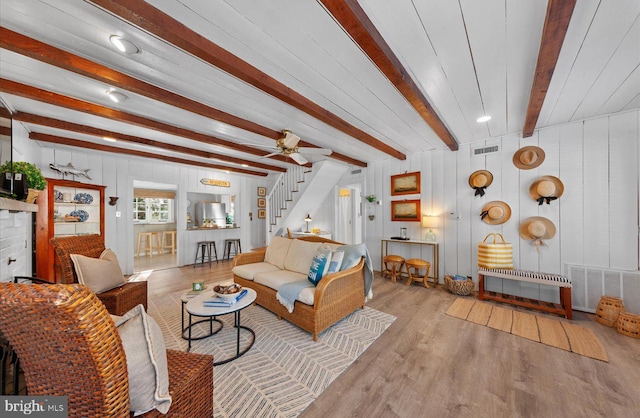 living room with ceiling fan, beam ceiling, light hardwood / wood-style flooring, and wooden walls