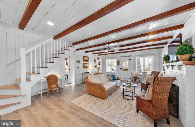 living room featuring light hardwood / wood-style floors, wood walls, ceiling fan, a brick fireplace, and beamed ceiling