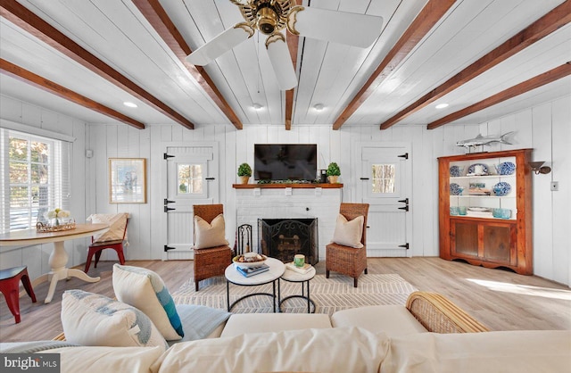 living room with a fireplace, beam ceiling, light hardwood / wood-style flooring, and ceiling fan