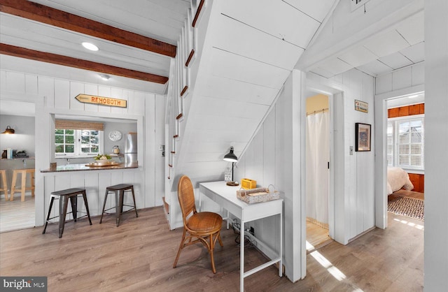 dining space with lofted ceiling with beams, wood walls, and light hardwood / wood-style flooring