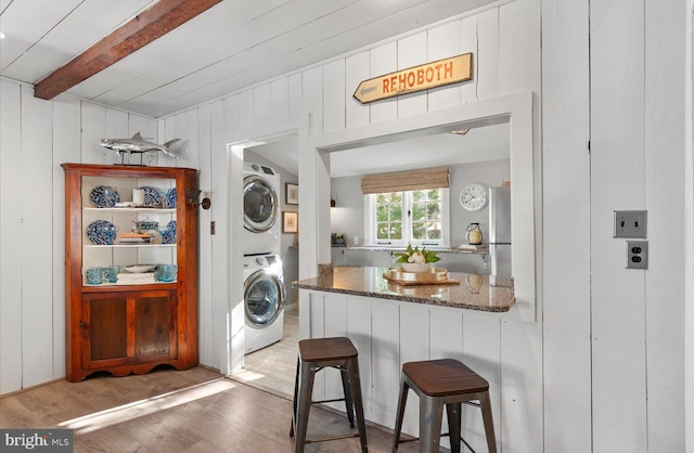 laundry room with stacked washer / drying machine, light wood-type flooring, and wood walls