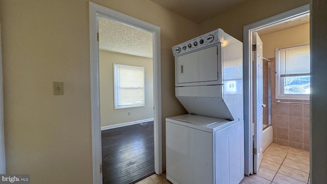 clothes washing area with light tile patterned floors, a textured ceiling, stacked washer and dryer, and a healthy amount of sunlight