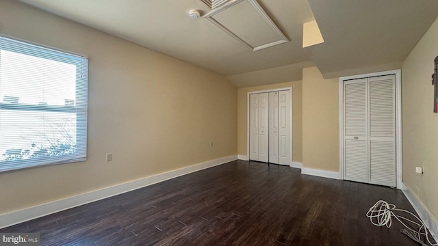 unfurnished bedroom featuring two closets, vaulted ceiling, dark hardwood / wood-style flooring, and multiple windows