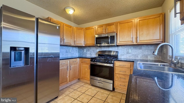 kitchen with sink, backsplash, a textured ceiling, light tile patterned floors, and appliances with stainless steel finishes