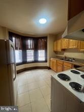 kitchen featuring stainless steel refrigerator, stove, light tile patterned floors, and ventilation hood