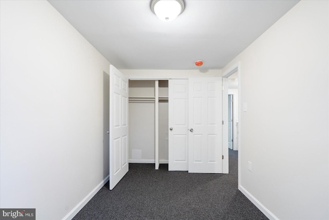 unfurnished bedroom with dark colored carpet and a closet