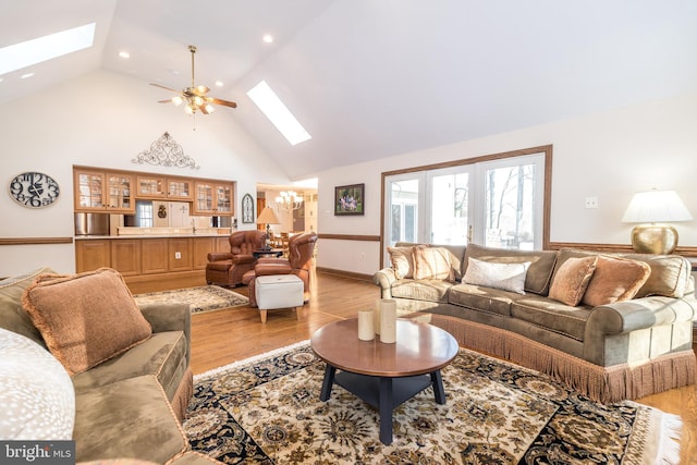 living room featuring light hardwood / wood-style flooring, ceiling fan with notable chandelier, a skylight, and high vaulted ceiling