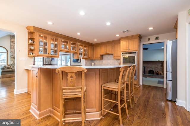 kitchen featuring a breakfast bar, wood-type flooring, appliances with stainless steel finishes, a fireplace, and decorative backsplash