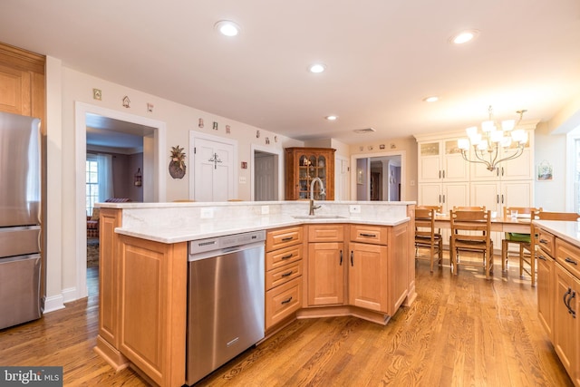 kitchen with sink, stainless steel appliances, hanging light fixtures, and a center island with sink