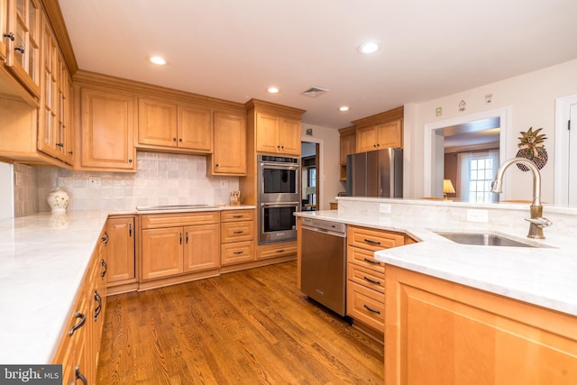 kitchen with dark wood-type flooring, sink, appliances with stainless steel finishes, light stone countertops, and decorative backsplash