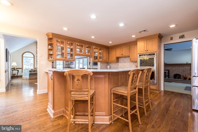 kitchen featuring dark hardwood / wood-style floors, tasteful backsplash, a breakfast bar area, a brick fireplace, and stainless steel double oven