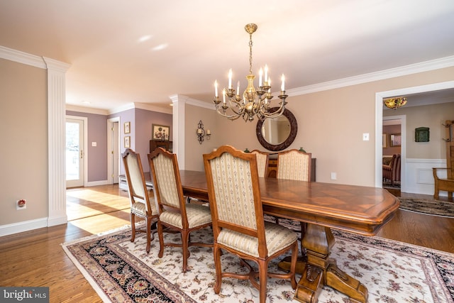 dining space featuring crown molding, wood-type flooring, a chandelier, and ornate columns