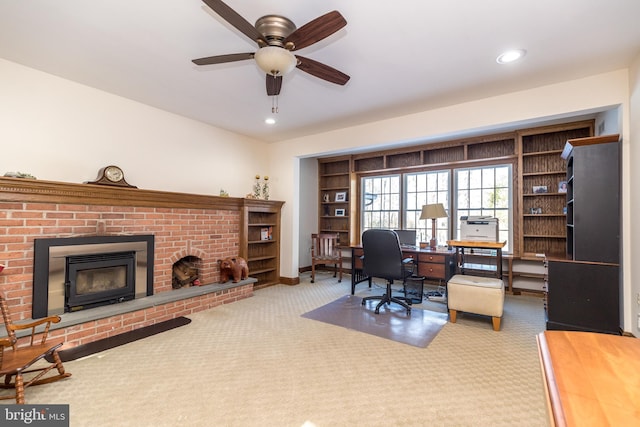 carpeted home office with a fireplace, built in features, and ceiling fan