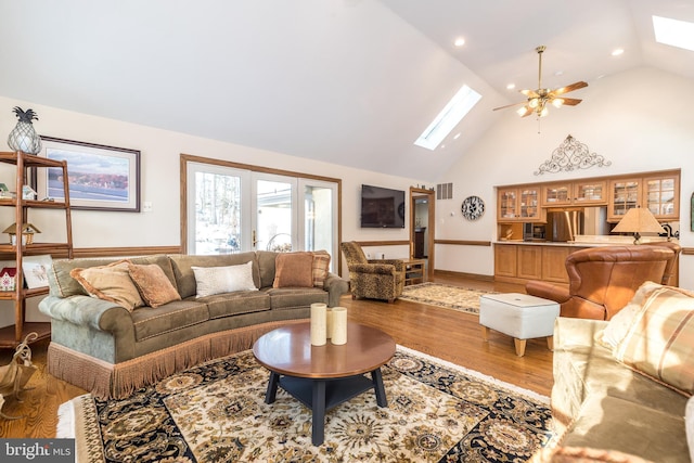 living room with hardwood / wood-style flooring, a skylight, high vaulted ceiling, and ceiling fan