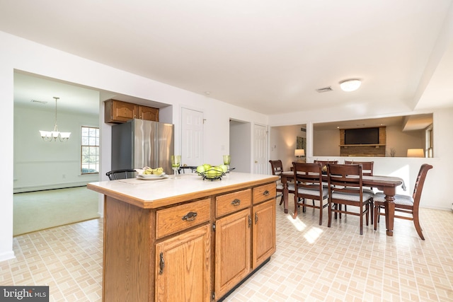 kitchen with hanging light fixtures, baseboard heating, a notable chandelier, a kitchen island, and stainless steel refrigerator