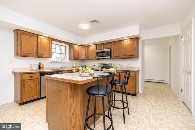 kitchen with a breakfast bar, stainless steel appliances, sink, a baseboard radiator, and a kitchen island