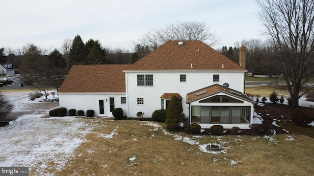 snow covered rear of property featuring a sunroom