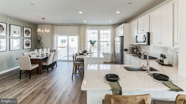 kitchen featuring appliances with stainless steel finishes, light stone counters, sink, pendant lighting, and white cabinets