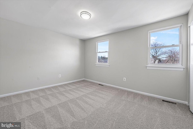 empty room featuring light carpet, visible vents, and baseboards