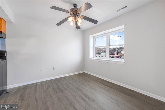 spare room featuring a ceiling fan, visible vents, wood finished floors, and baseboards