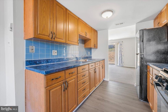 kitchen featuring dark countertops, backsplash, light wood-type flooring, stove, and a sink