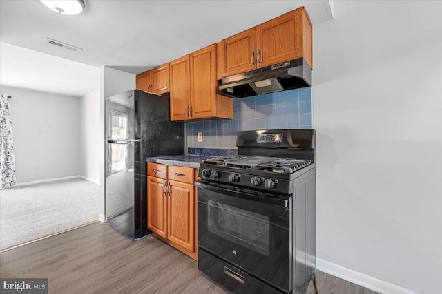 kitchen featuring visible vents, black appliances, under cabinet range hood, tasteful backsplash, and light wood-style floors