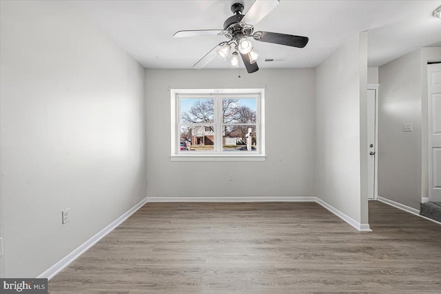 spare room featuring ceiling fan, visible vents, baseboards, and wood finished floors