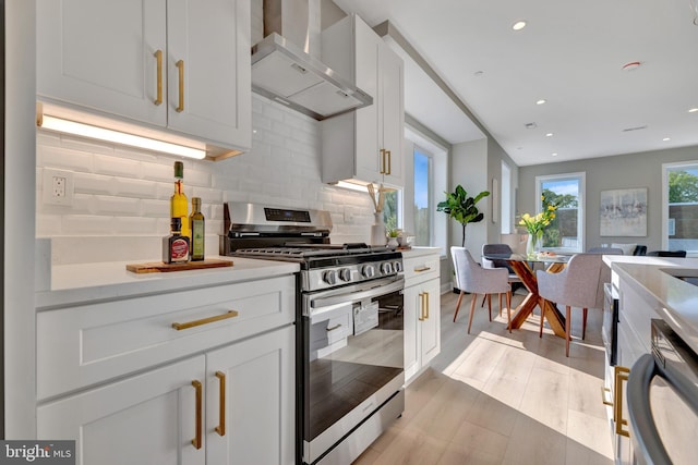 kitchen featuring tasteful backsplash, dishwashing machine, gas stove, wall chimney range hood, and white cabinets