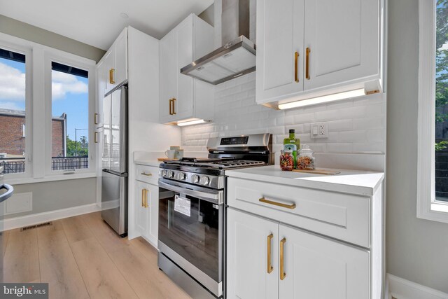 kitchen featuring wall chimney exhaust hood, stainless steel appliances, backsplash, light hardwood / wood-style floors, and white cabinets