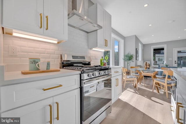 kitchen featuring white cabinets, decorative backsplash, stainless steel gas stove, and wall chimney exhaust hood