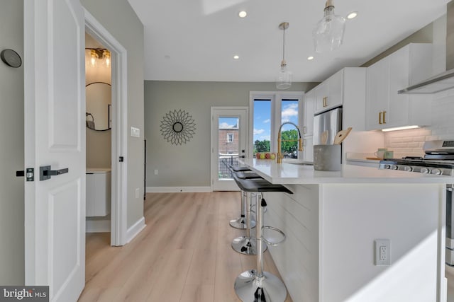 kitchen with white cabinets, wall chimney exhaust hood, decorative light fixtures, a kitchen bar, and stainless steel appliances