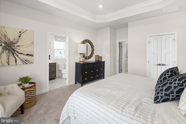 bedroom with ensuite bath, a tray ceiling, light colored carpet, and a closet