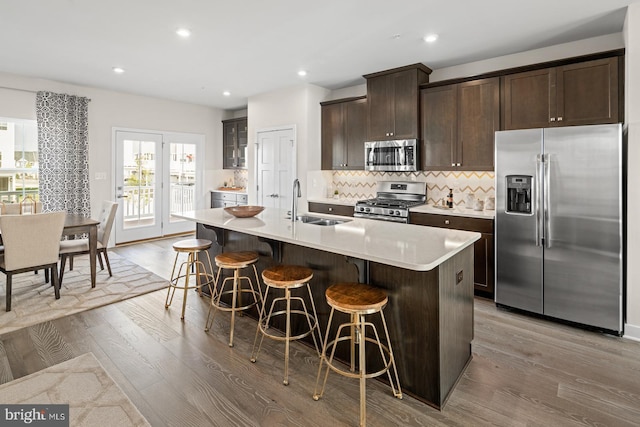 kitchen featuring stainless steel appliances, a kitchen island with sink, a kitchen bar, and light wood-type flooring