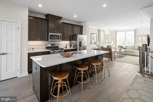 kitchen with a kitchen island with sink, a kitchen bar, light wood-type flooring, and appliances with stainless steel finishes