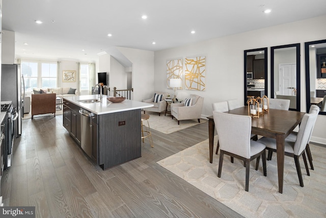 kitchen with a breakfast bar, sink, a kitchen island with sink, light hardwood / wood-style floors, and stainless steel appliances