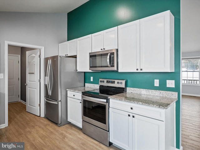 kitchen with light stone countertops, appliances with stainless steel finishes, white cabinets, and light hardwood / wood-style flooring