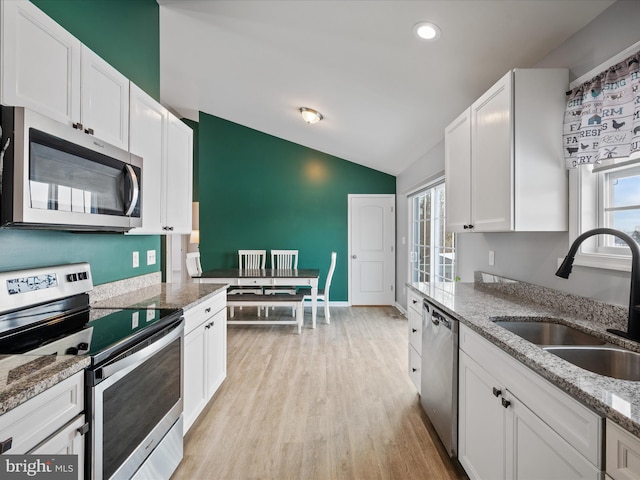 kitchen featuring lofted ceiling, sink, light stone counters, stainless steel appliances, and white cabinets