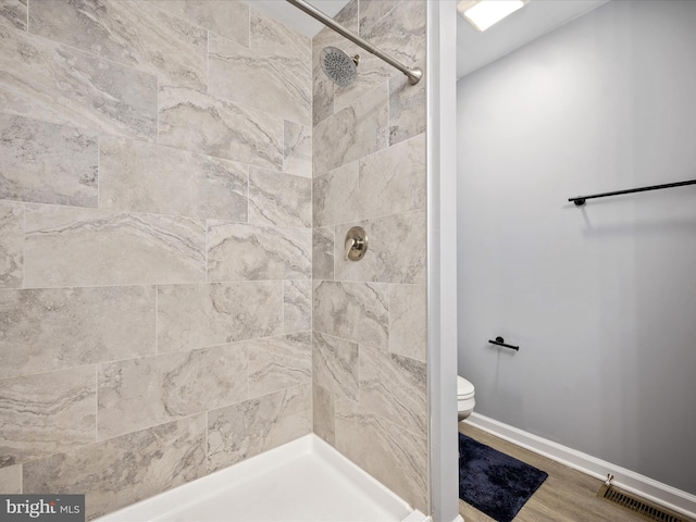 bathroom featuring hardwood / wood-style flooring, tiled shower, and toilet