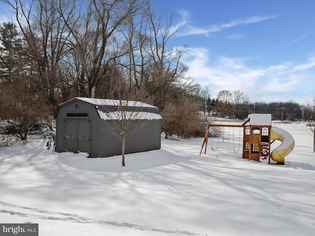 snowy yard with a storage shed and a playground