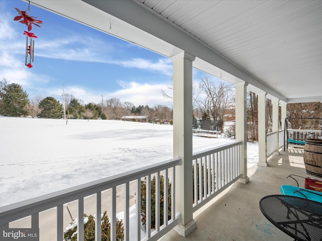 snow covered back of property featuring covered porch