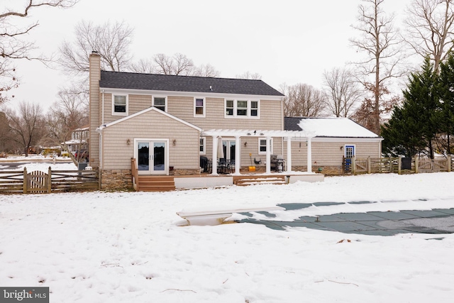 snow covered back of property featuring french doors and a pergola