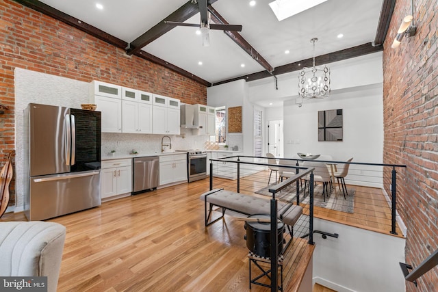 kitchen with white cabinetry, decorative light fixtures, appliances with stainless steel finishes, light hardwood / wood-style floors, and wall chimney range hood