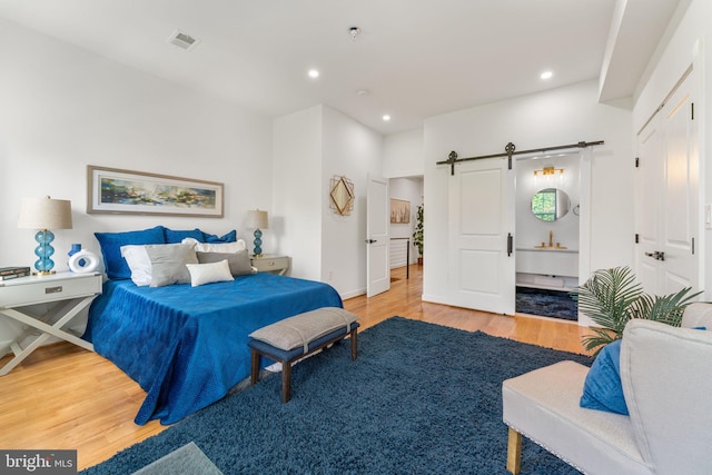 bedroom with connected bathroom, a barn door, and hardwood / wood-style floors