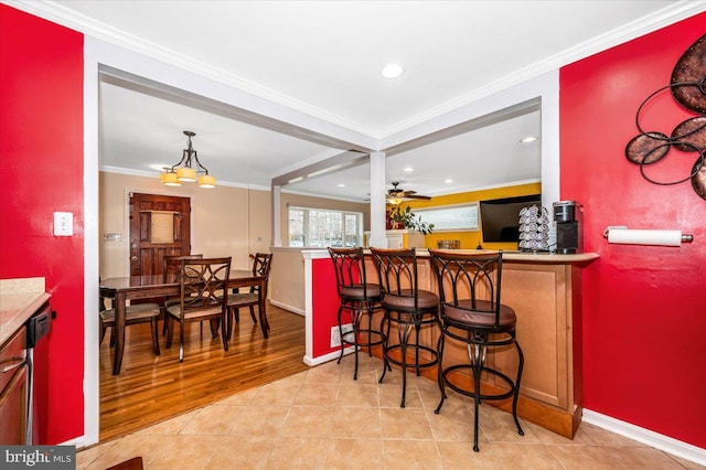 dining room with crown molding, light tile patterned floors, a ceiling fan, a bar, and baseboards