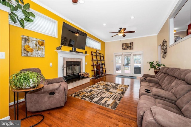 living area featuring french doors, ornamental molding, a ceiling fan, wood finished floors, and a tile fireplace