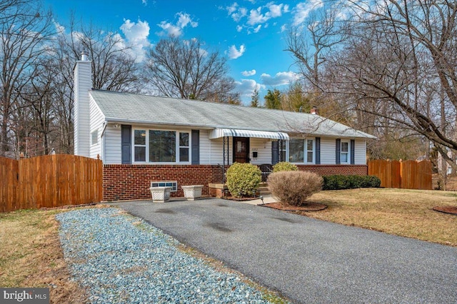 view of front facade featuring brick siding, fence, driveway, a chimney, and a front yard