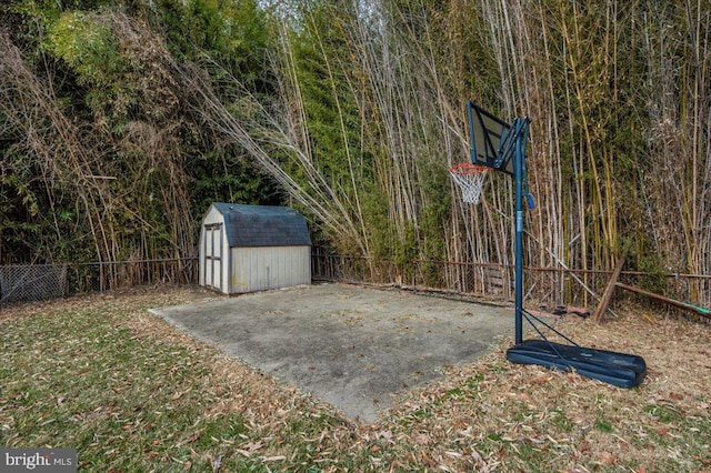 view of patio / terrace featuring basketball hoop, fence, an outdoor structure, and a storage unit