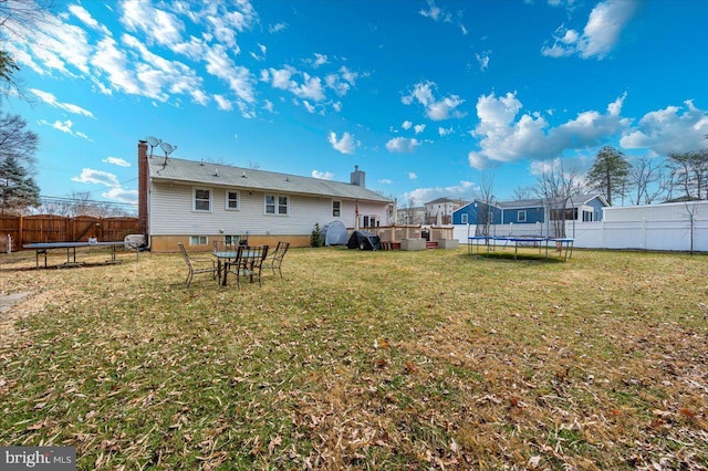 rear view of property featuring a fenced backyard, a trampoline, and a lawn