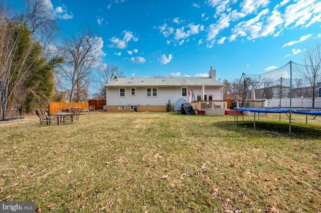 back of house featuring a trampoline, a yard, fence, and a wooden deck